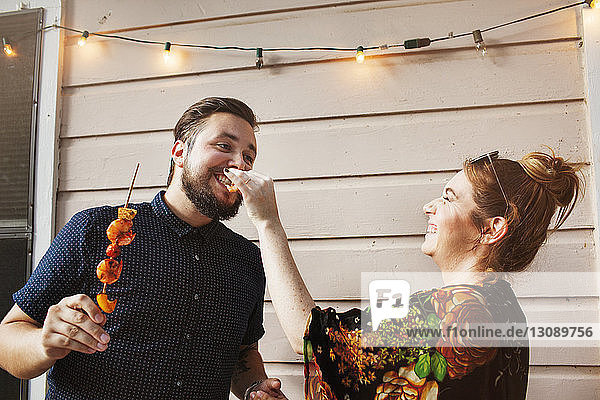 Glückliche Frau füttert Freundin mit Garnelen  während sie an der Wand steht