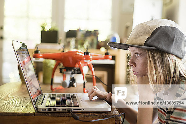 Seitenansicht eines Jungen  der zu Hause mit einer Drohne am Laptop arbeitet