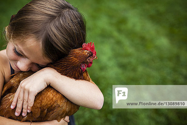 Hochwinkelansicht eines süßen Mädchens  das die Henne im Hof umarmt