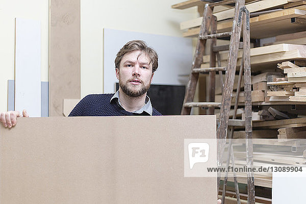Portrait of carpenter holding wooden planks in workshop