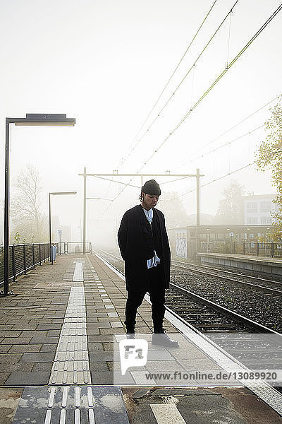 Full length of man standing on railroad station platform in foggy weather