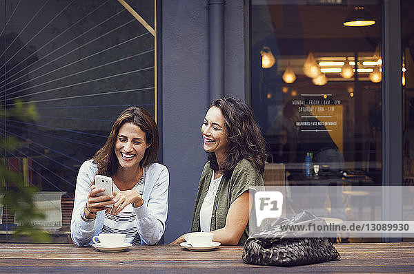Glückliche Freundinnen mit Smartphone im Straßencafé