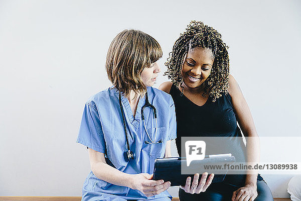 Arzt zeigt einer schwangeren Frau Ultraschall am Tablet-Computer  während sie vor weißem Hintergrund sitzt