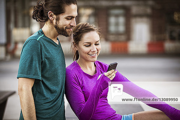 Glückliche Frau zeigt einem Freund ihr Handy  während sie auf einer Bank sitzt