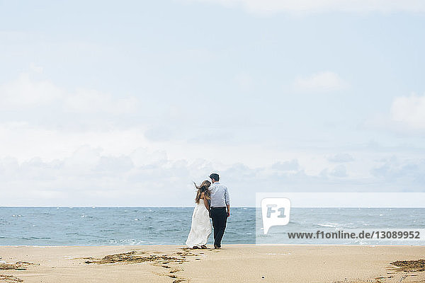 Rückansicht eines am Strand stehenden frisch vermählten Paares gegen den Himmel