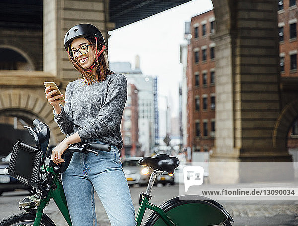 Happy woman using smart phone while standing by bicycle on street