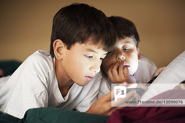 Brothers looking in phone while resting on bed at home