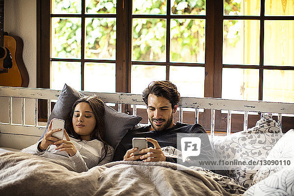 Ehepaar benutzt Smartphones  während es zu Hause im Bett liegt