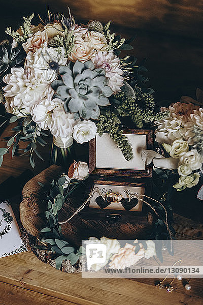Nahaufnahme der Eheringe inmitten eines Kranzes durch einen Blumenstrauss auf dem Tisch