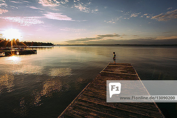 High angle view of shirtless boy standing on jetty against sky during sunset