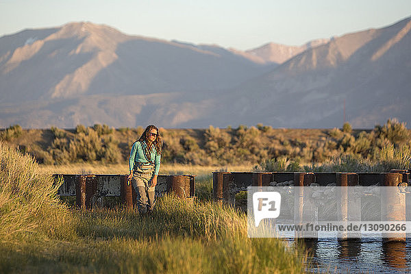 Young woman with fishing rod standing in Owens River against mountains