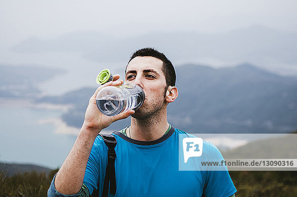Männlicher Wanderer trinkt Wasser  während er auf Berg gegen Himmel steht