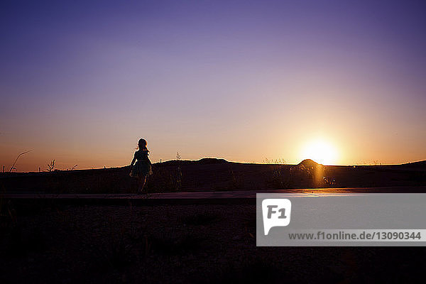Silhouette girl standing at park against sky during sunset
