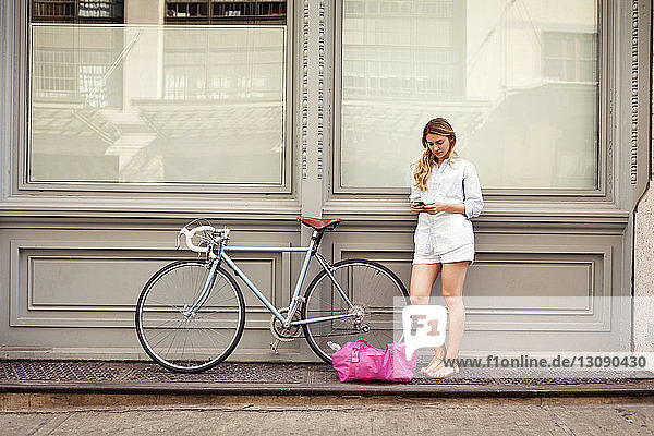 Frau telefoniert  während sie mit dem Fahrrad auf dem Bürgersteig in der Stadt steht