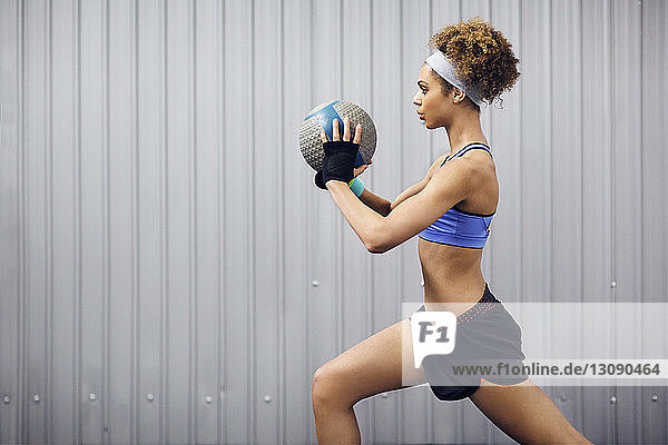 Side view of determined female athlete exercising with medicine ball in gym