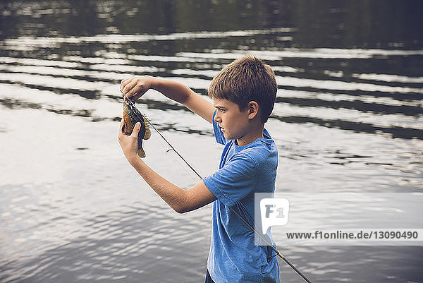 Seitenansicht eines Jungen  der am See Fische von der Angelrute entfernt