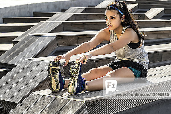 Female athlete exercising while sitting on wooden seat