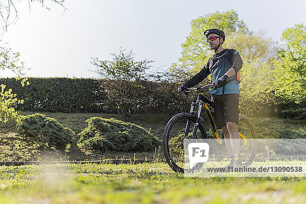 Full length of young man with mountain bike standing on field at park