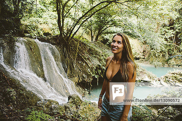 Smiling young woman wearing bikini top while standing in forest