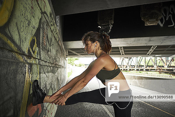 Woman stretching leg on graffiti wall while exercising