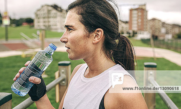 Frau schaut weg  während sie eine Wasserflasche im Park hält