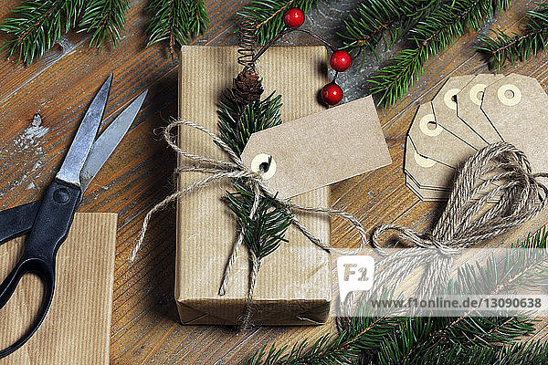 Schrägansicht eines Weihnachtsgeschenks mit Etiketten und Schnüren durch Kiefernnadeln auf Holztisch