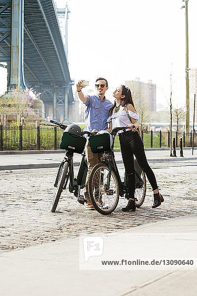 Couple taking selfie while standing with bicycles on street