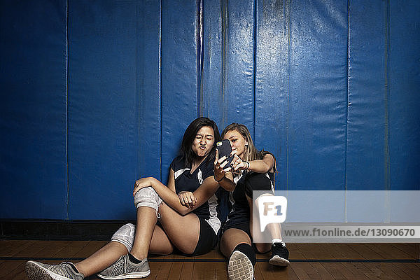 Mädchen  die auf dem Boden sitzen und mit einem Smartphone auf Selfie klicken