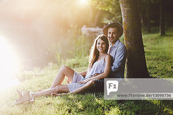 Porträt eines Paares  das auf einem Grasfeld bei einem Baum im Park sitzt