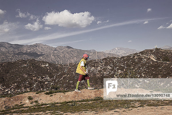 Side view of boy walking on field against mountains and sky