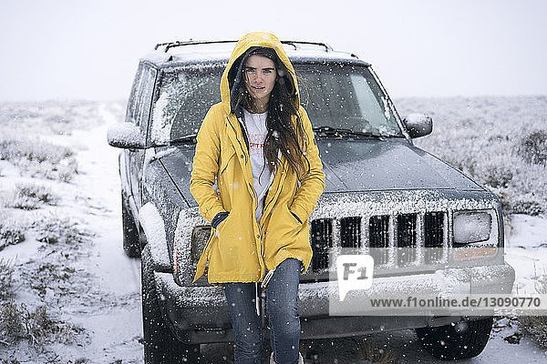 Porträt einer Frau  die im Winter auf dem Feld neben einem Geländewagen steht