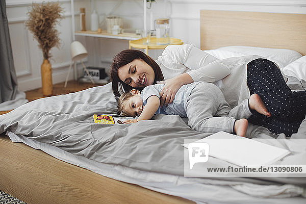 Happy mother lying with baby boy in bed at home
