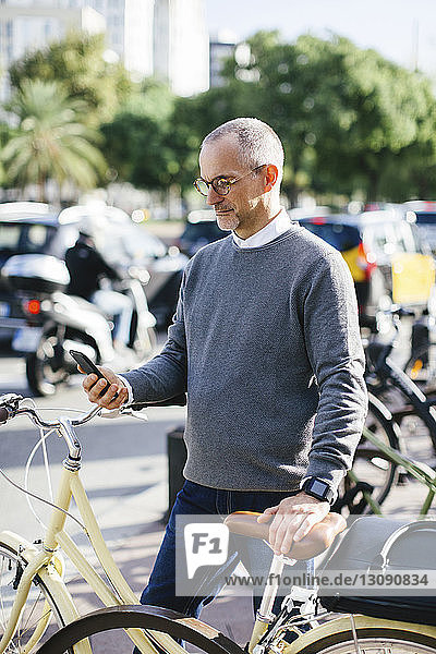 Businessman using smart phone while standing by bicycle in city