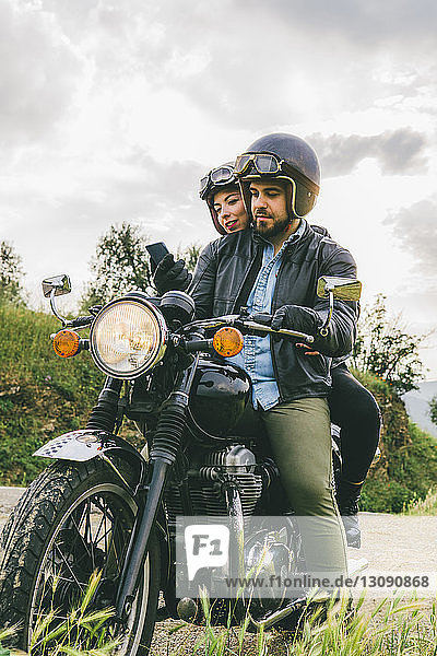 Ehepaar benutzt Mobiltelefon  während es auf einem Motorrad gegen den Himmel sitzt