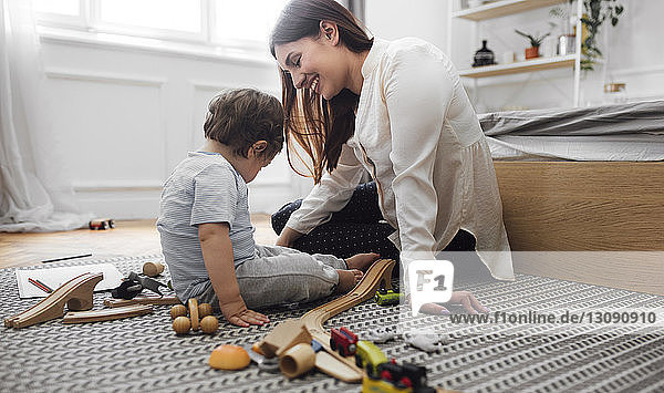Happy mother and baby boy playing with toys on rug at home