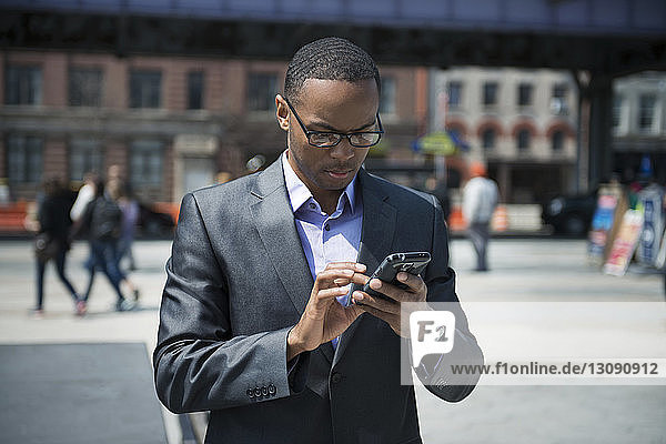 Frontansicht eines Geschäftsmannes  der ein Smartphone auf der Straße benutzt