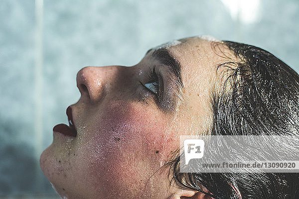 Nahaufnahme einer nassen  geschminkten jungen Frau  die beim Baden im häuslichen Badezimmer aufschaut