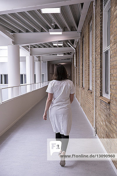 Rear view of female doctor walking in hospital corridor