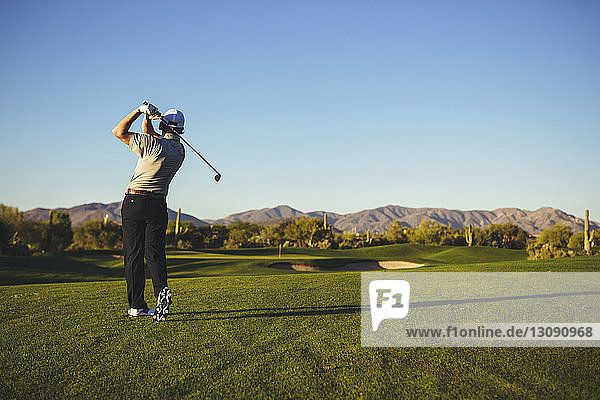Rear view of man playing golf against clear blue sky