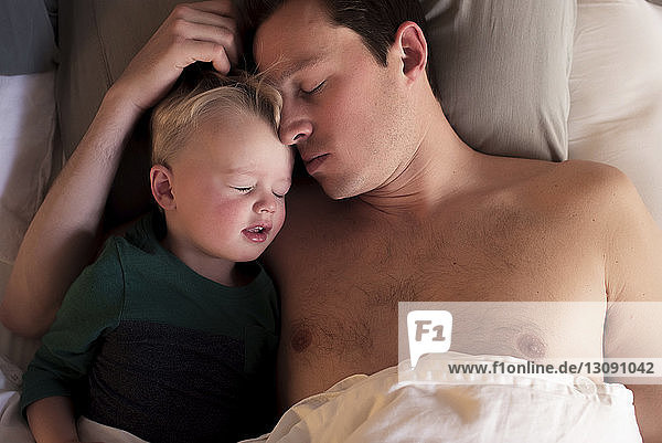Hochwinkelaufnahme von Vater und Sohn  die zu Hause auf dem Bett schlafen