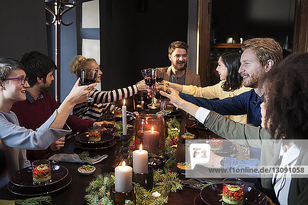 Friends toasting wine while enjoying meal at Christmas party