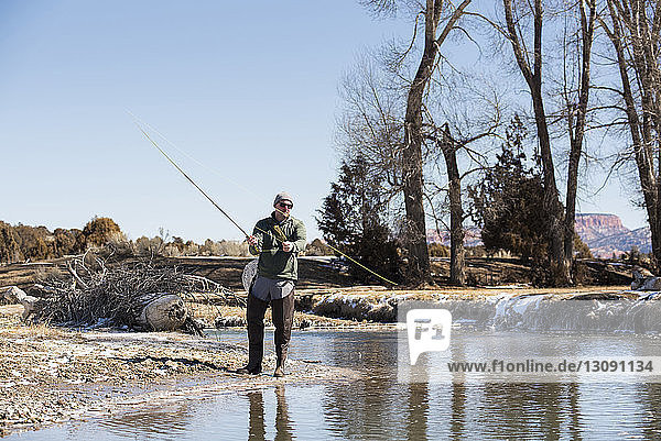 Mann in voller Länge fischt im Fluss gegen klaren Himmel