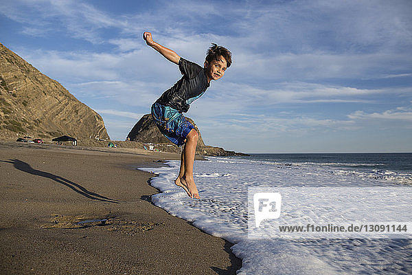 Portrait of boy jumping in surf at beach against sky