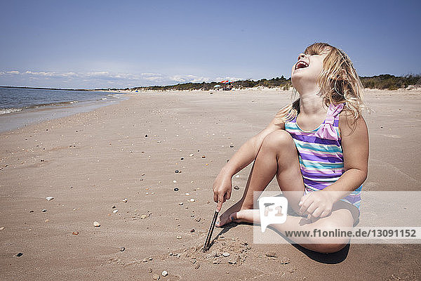 Glückliches Mädchen mit dem Kopf nach hinten auf Sand am Strand sitzend