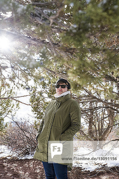 Woman with hands in winter coat's pockets standing by branches at desert during winter