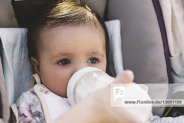 Abgehackte Hand einer Mutter  die ihre im Kinderwagen sitzende Tochter mit Milch füttert