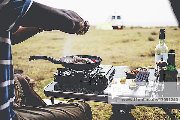 Ausgeschnittenes Bild eines Mannes  der auf einem Campingkocher auf dem Campingplatz Essen zubereitet