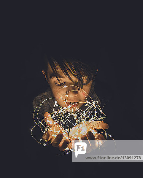 Close-up of boy holding illuminated string lights in darkroom