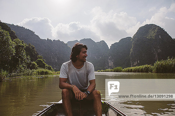 Man looking away while sitting in boat on river against sky