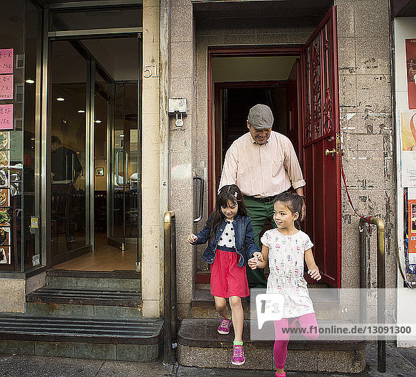 Happy grandfather with grandchildren walking out of store in city